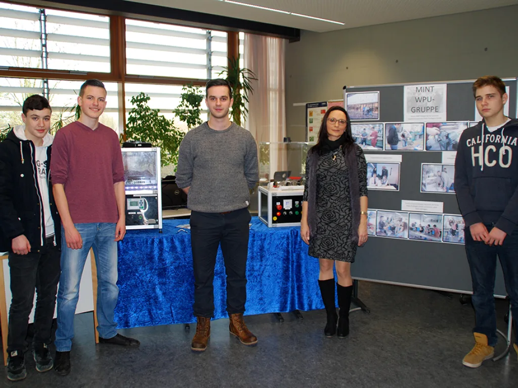 Fünf Personen stehen vor einer Stellwand mit Fotos.